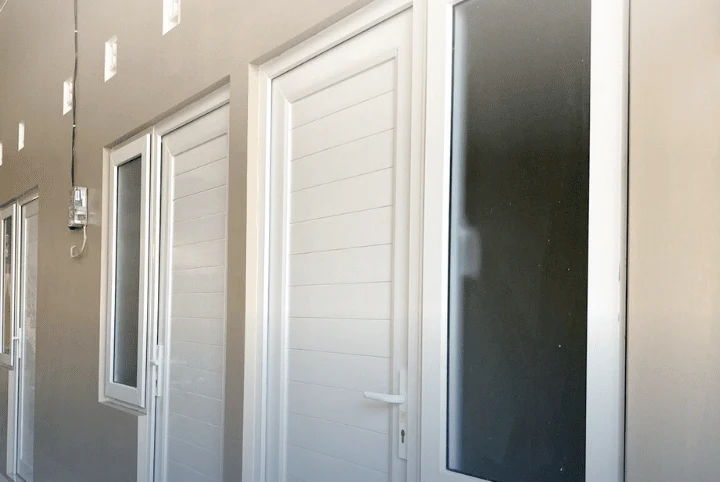Pintu UPVC putih berpanel pada deretan kamar di bangunan kos